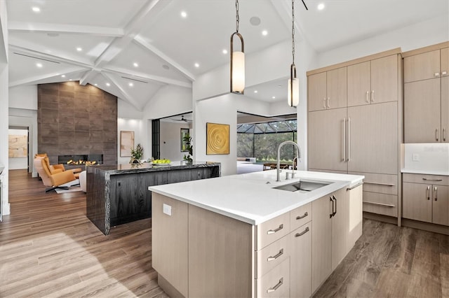 kitchen with sink, a tile fireplace, light brown cabinets, an island with sink, and light wood-type flooring