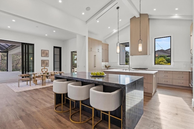 kitchen with beam ceiling, a kitchen island, light brown cabinetry, decorative light fixtures, and light wood-type flooring