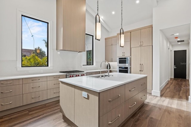 kitchen featuring light brown cabinetry, sink, hanging light fixtures, appliances with stainless steel finishes, and an island with sink