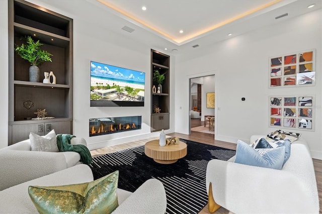 living room featuring a tray ceiling, hardwood / wood-style flooring, and built in features