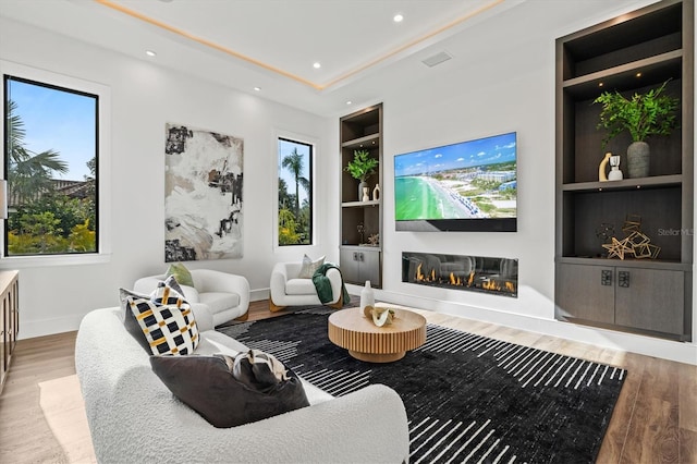 living room with built in shelves, plenty of natural light, and hardwood / wood-style flooring