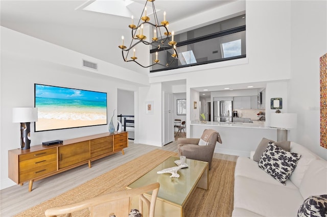 living room featuring a high ceiling, a notable chandelier, light wood-type flooring, and a skylight