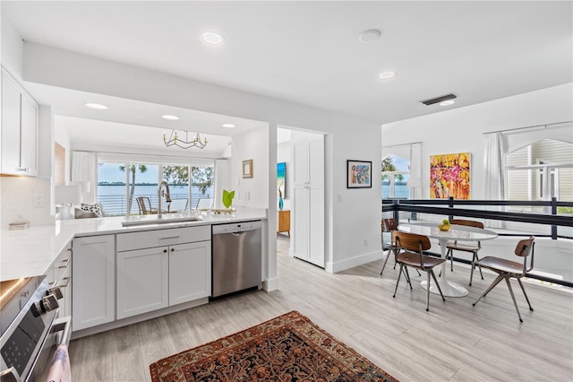 kitchen featuring sink, appliances with stainless steel finishes, white cabinetry, a water view, and a healthy amount of sunlight