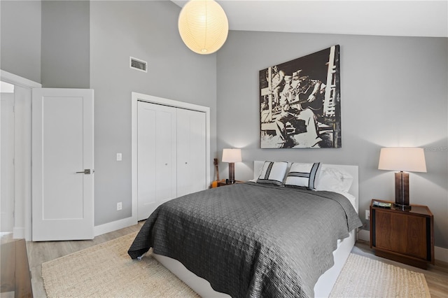 bedroom with high vaulted ceiling, light hardwood / wood-style floors, and a closet