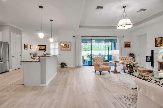 kitchen with crown molding, stainless steel refrigerator, stone countertops, decorative light fixtures, and light wood-type flooring