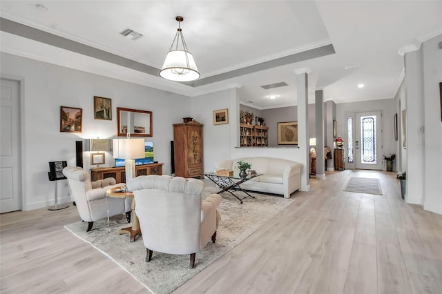 living room featuring decorative columns, crown molding, light hardwood / wood-style flooring, and a tray ceiling