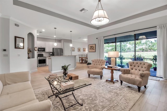 living room with a tray ceiling, ornamental molding, and light hardwood / wood-style floors