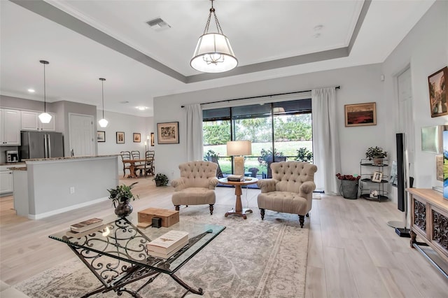 living room with ornamental molding, a tray ceiling, and light hardwood / wood-style floors