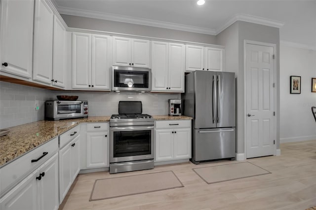 kitchen with white cabinetry, ornamental molding, appliances with stainless steel finishes, and light stone counters