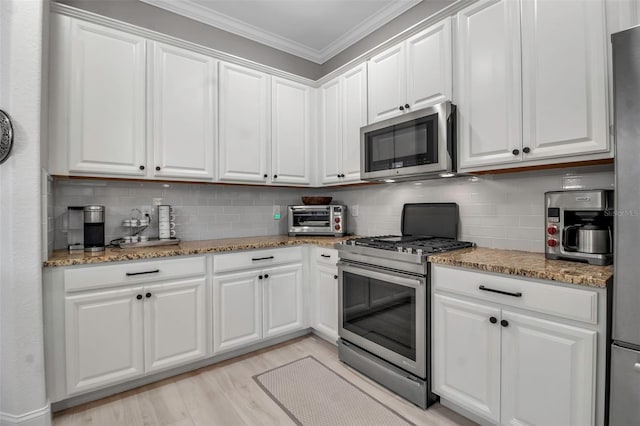 kitchen with stone counters, appliances with stainless steel finishes, white cabinets, ornamental molding, and light hardwood / wood-style flooring