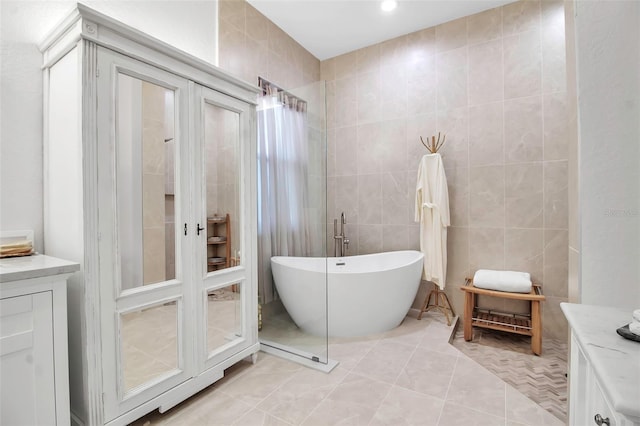 bathroom featuring vanity, a tub to relax in, tile patterned floors, and tile walls