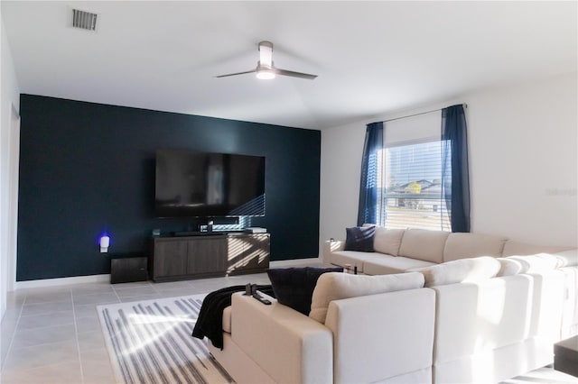 living area with light tile patterned floors, visible vents, baseboards, ceiling fan, and an accent wall