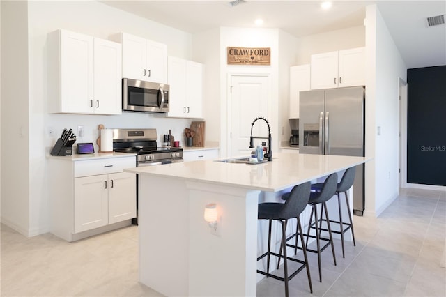 kitchen with stainless steel appliances, white cabinets, light countertops, and a center island with sink