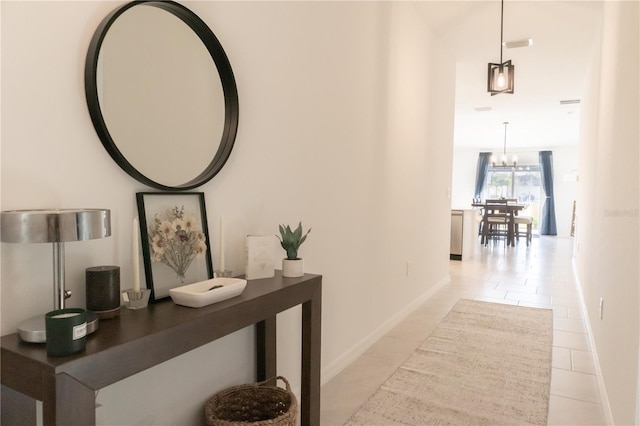 hallway with baseboards, a notable chandelier, and light tile patterned flooring