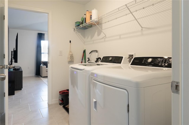 washroom featuring light tile patterned floors, laundry area, separate washer and dryer, and baseboards