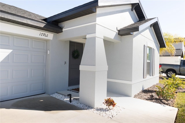 view of exterior entry featuring a garage, roof with shingles, and stucco siding