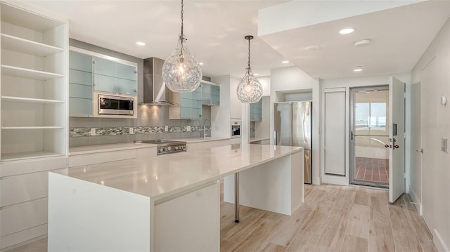 kitchen featuring hanging light fixtures, appliances with stainless steel finishes, light countertops, a center island, and wall chimney exhaust hood