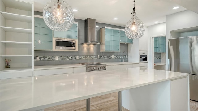 kitchen featuring wall chimney exhaust hood, modern cabinets, a center island, stainless steel appliances, and light countertops