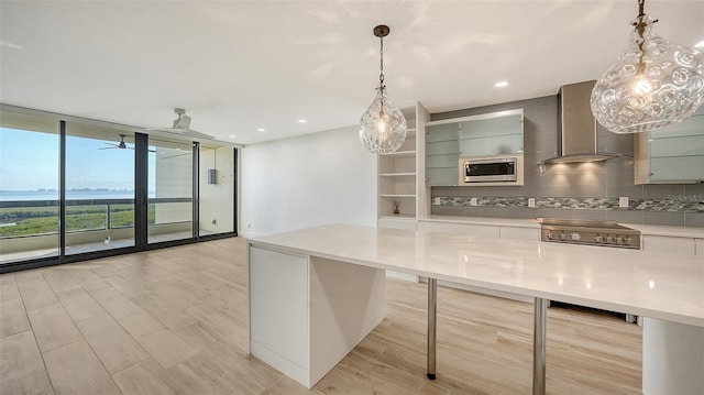 kitchen with wall chimney exhaust hood, stainless steel microwave, expansive windows, light countertops, and pendant lighting