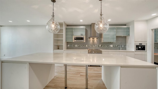 kitchen featuring light countertops, decorative light fixtures, a kitchen island, and wall chimney exhaust hood