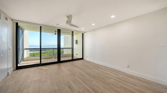 spare room featuring a water view, light wood-style flooring, baseboards, and a wall of windows