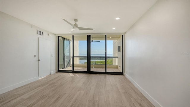 spare room with a water view, visible vents, light wood-style floors, expansive windows, and baseboards