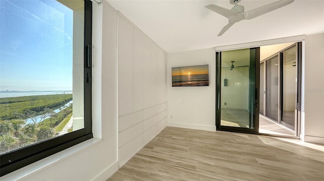 corridor featuring light wood-style floors, a water view, and baseboards