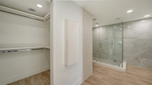 full bathroom featuring a marble finish shower, a spacious closet, visible vents, and wood finished floors