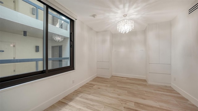 empty room featuring light wood-style flooring, visible vents, a chandelier, and baseboards