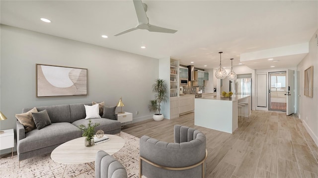 living room featuring baseboards, a ceiling fan, light wood-style flooring, and recessed lighting