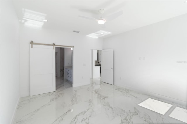 unfurnished bedroom featuring a barn door, connected bathroom, and ceiling fan