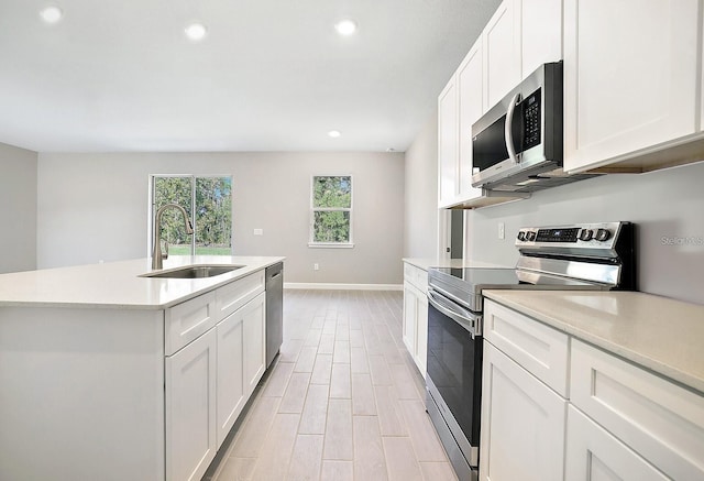 kitchen with sink, light hardwood / wood-style flooring, appliances with stainless steel finishes, white cabinetry, and an island with sink