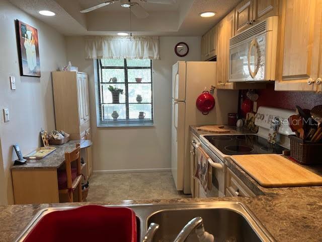 kitchen with white appliances, a raised ceiling, and ceiling fan