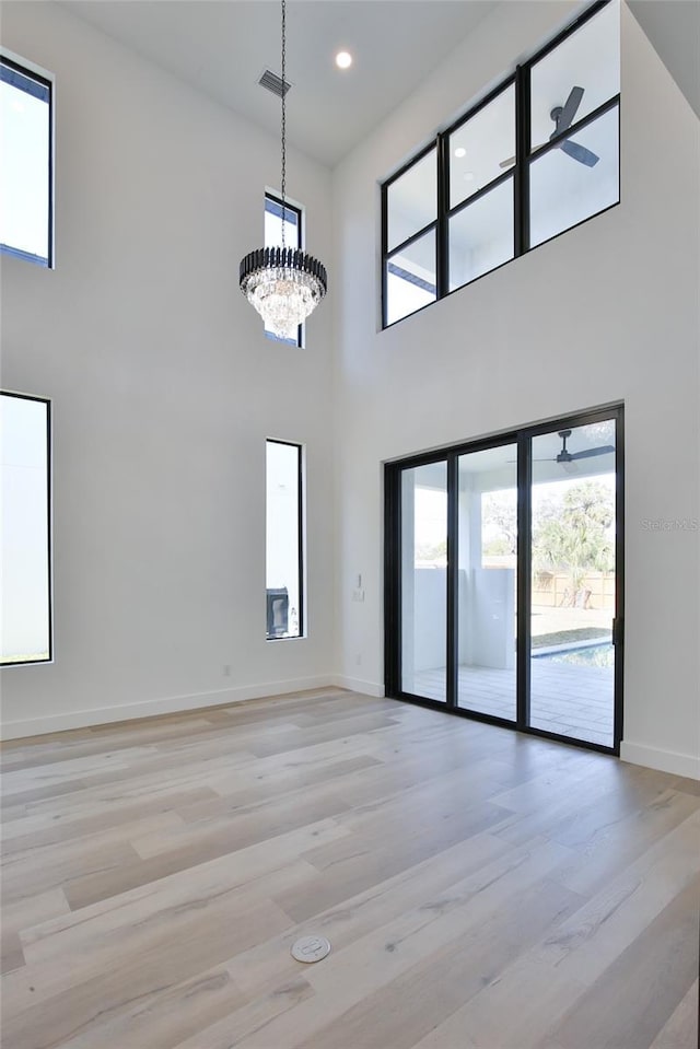 unfurnished room with a notable chandelier, a high ceiling, and light wood-type flooring