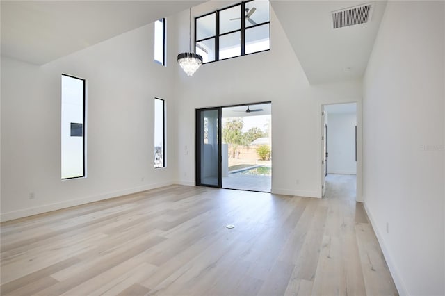 unfurnished room with a high ceiling, an inviting chandelier, and light hardwood / wood-style flooring