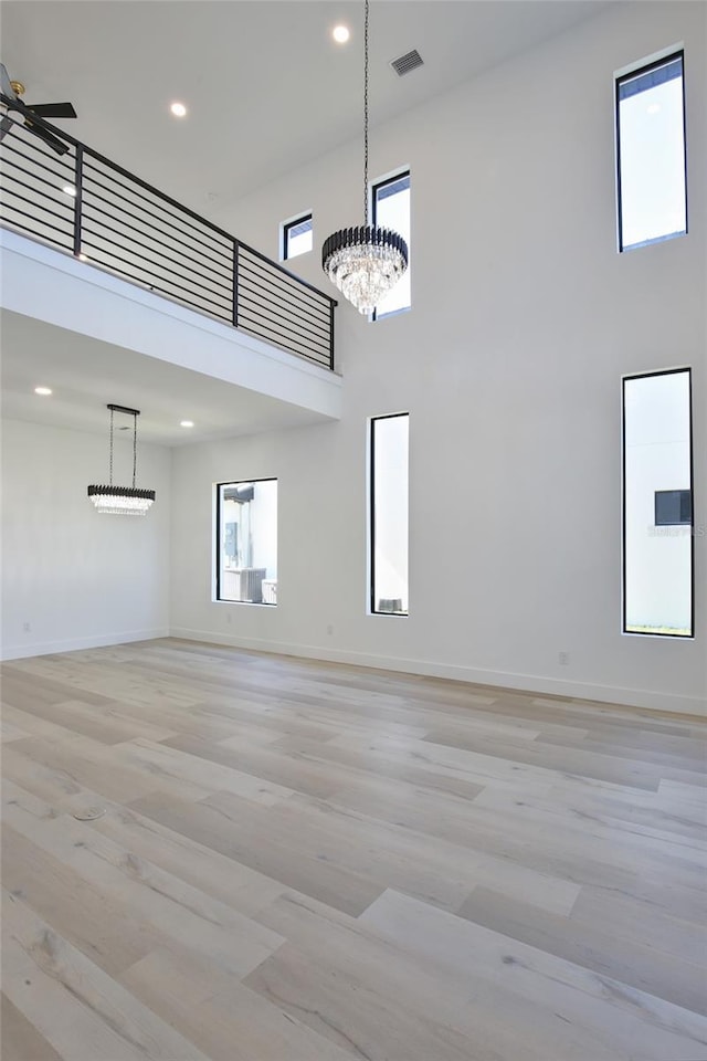 unfurnished living room featuring a towering ceiling, ceiling fan with notable chandelier, and light wood-type flooring