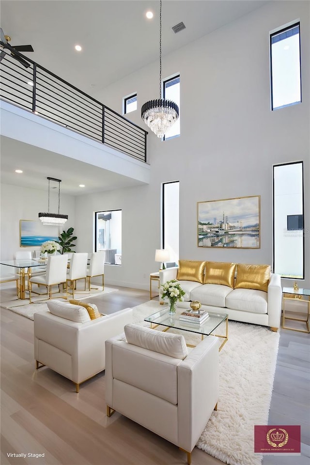 living room with a notable chandelier, light hardwood / wood-style flooring, and a high ceiling