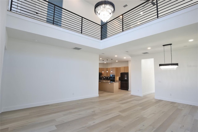 unfurnished living room featuring a high ceiling, a notable chandelier, and light hardwood / wood-style flooring