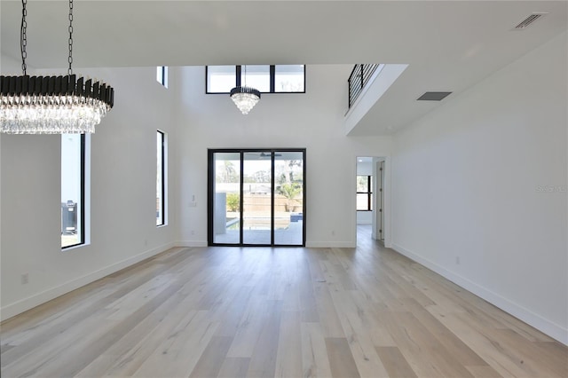 unfurnished room featuring an inviting chandelier, a towering ceiling, and light hardwood / wood-style flooring