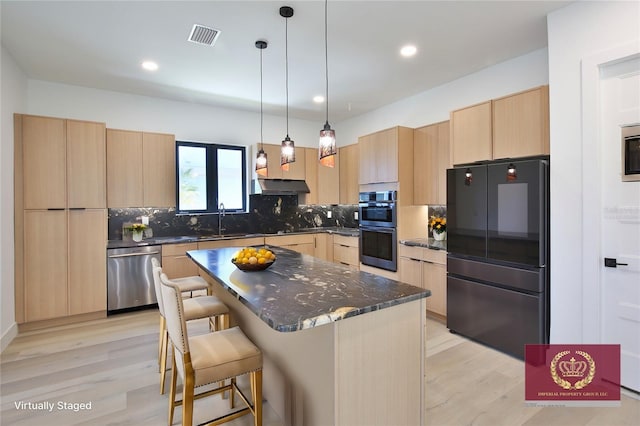 kitchen featuring sink, stainless steel appliances, a center island, light brown cabinetry, and dark stone counters