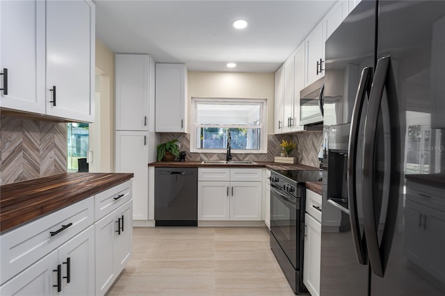 kitchen featuring butcher block countertops, sink, white cabinetry, backsplash, and black appliances