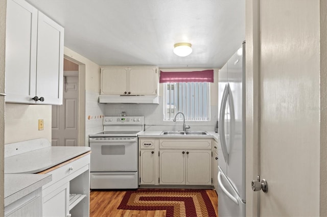 kitchen featuring sink, white appliances, wood-type flooring, white cabinets, and decorative backsplash