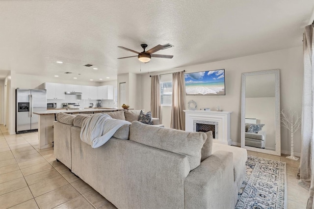 tiled living room featuring ceiling fan, a premium fireplace, and a textured ceiling