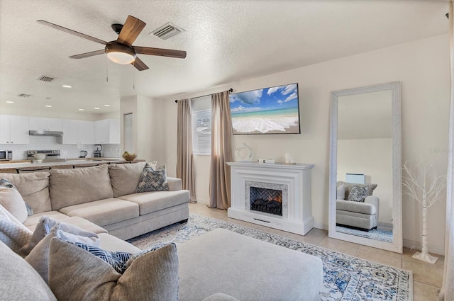 tiled living room featuring ceiling fan, a textured ceiling, and a high end fireplace