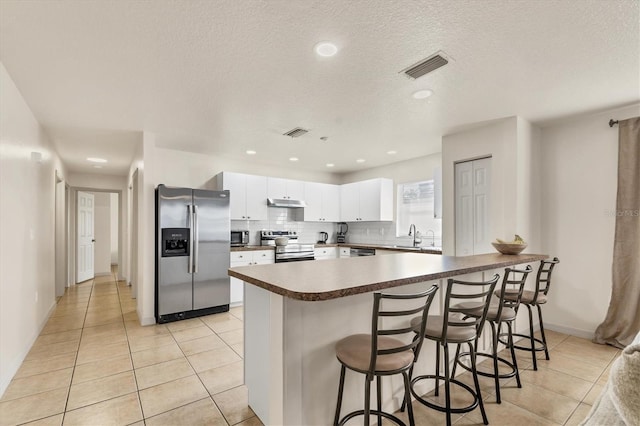 kitchen with a breakfast bar area, white cabinetry, backsplash, stainless steel appliances, and light tile patterned flooring