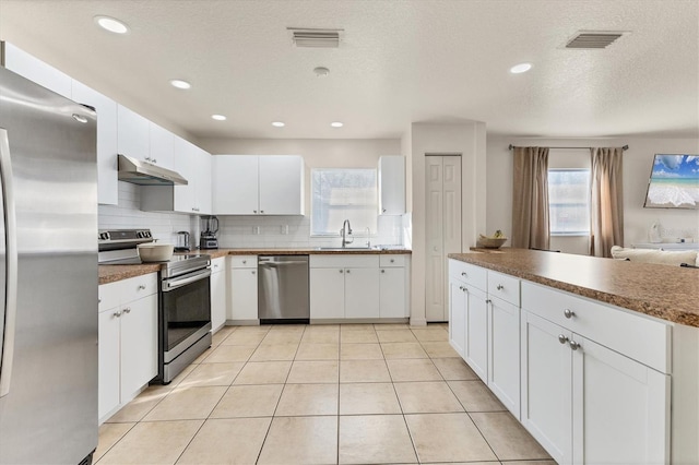 kitchen featuring white cabinetry, sink, decorative backsplash, light tile patterned floors, and stainless steel appliances