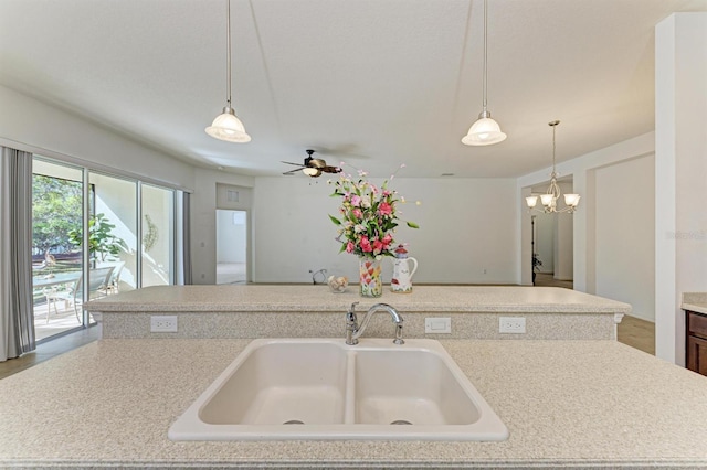 kitchen with decorative light fixtures, open floor plan, light countertops, ceiling fan with notable chandelier, and a sink