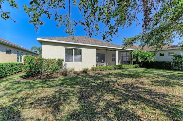 back of property with a lawn, a sunroom, and stucco siding