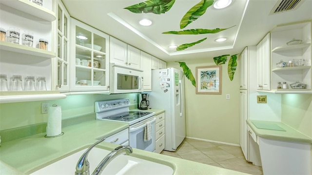 kitchen with sink, white appliances, white cabinets, light tile patterned flooring, and a raised ceiling