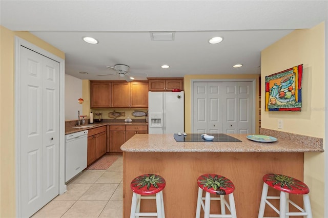 kitchen with light tile patterned flooring, a breakfast bar, white appliances, and kitchen peninsula